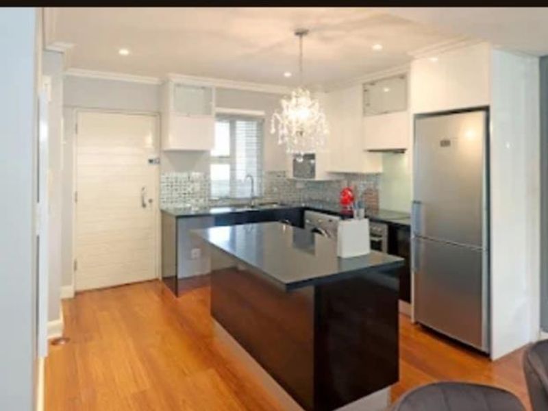 Modern kitchen featuring a central island, stone countertops, built-in cabinetry, and high-quality hardwood flooring, offering a functional and stylish cooking space.