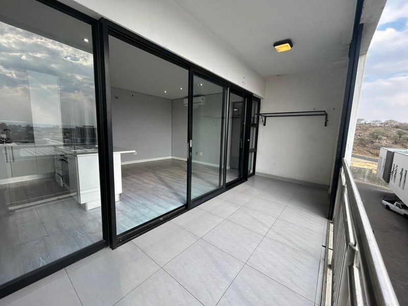 A spacious covered balcony featuring modern tiled flooring, a metal balustrade, and large sliding glass doors providing access to the interior living area.