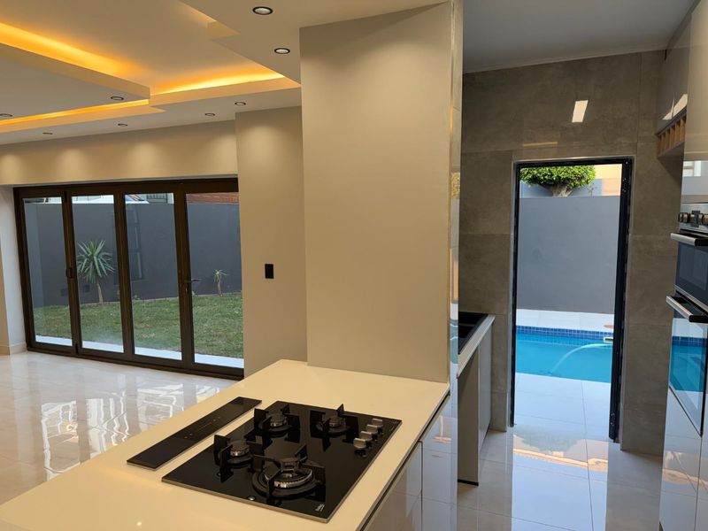 Modern open-plan kitchen area featuring a gas hob, built-in oven, and sleek tiled flooring, with direct access to the outdoor pool and garden area.
