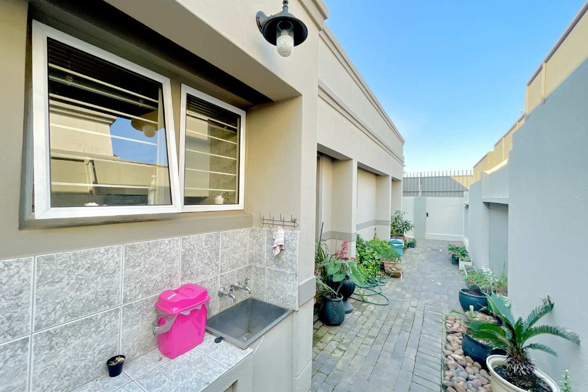 A paved rear exterior area featuring a built-in tiled wash basin, external lighting, and secure boundary walls.