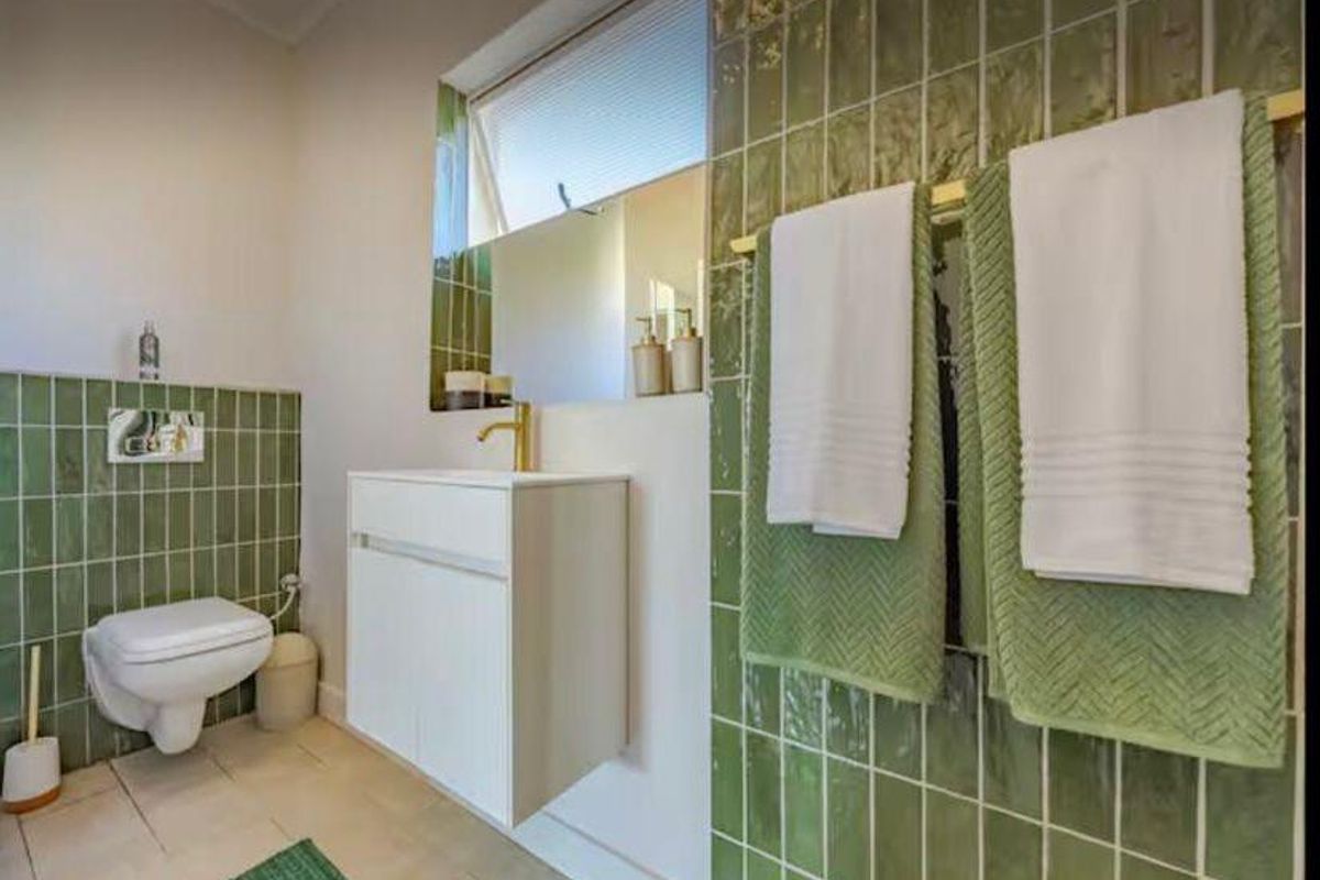 A modern bathroom featuring green subway-style wall tiles, a wall-mounted vanity with a gold faucet, and a wall-hung toilet.