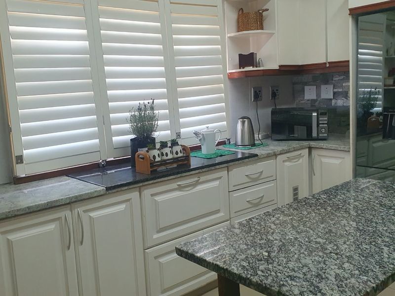 A well-maintained kitchen featuring granite countertops, white shaker-style cabinetry, and plantation shutters, offering a functional and classic workspace.