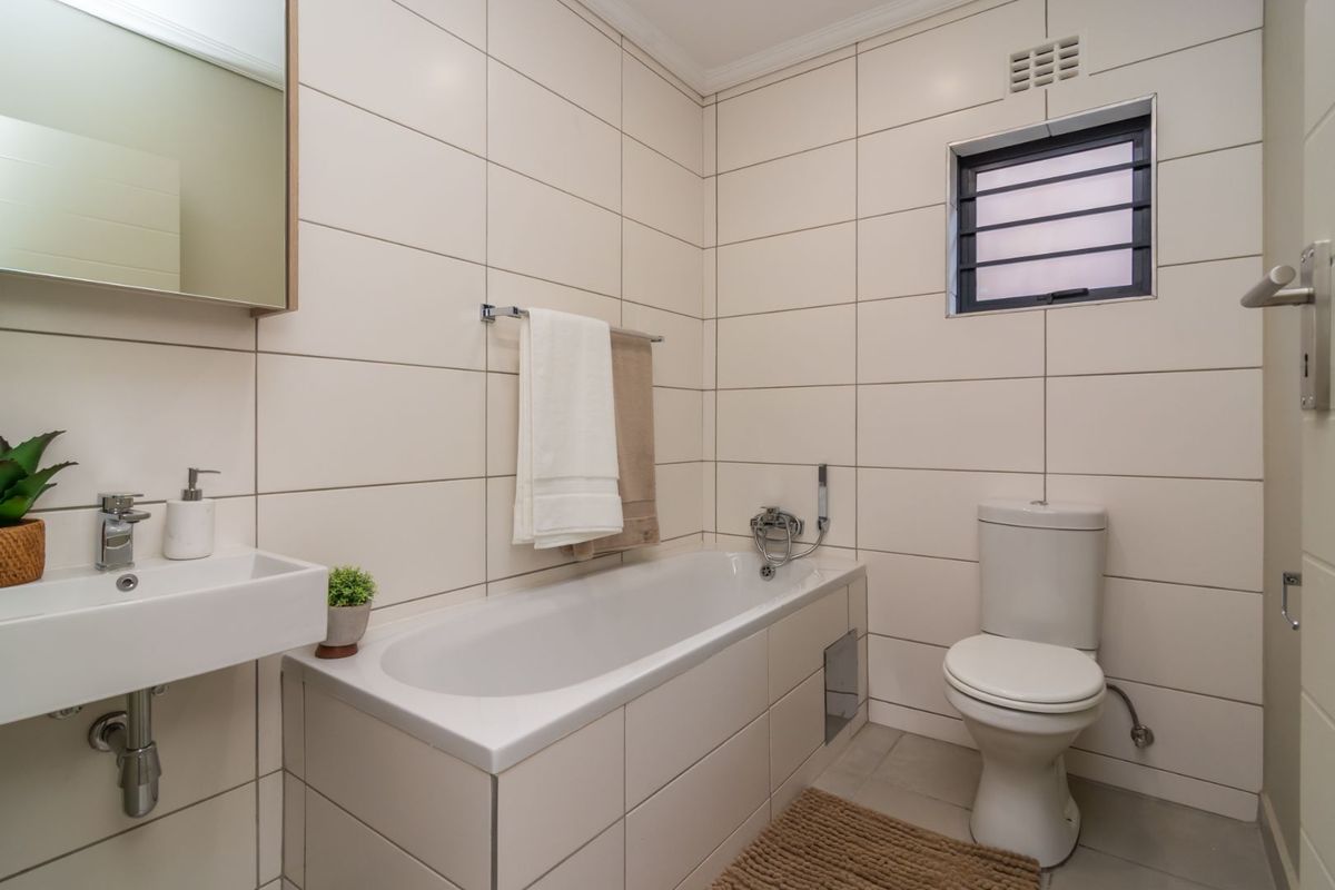 A clean, modern bathroom featuring tiled walls, a built-in bathtub with a handheld shower, a wall-mounted basin, and a close-coupled toilet.