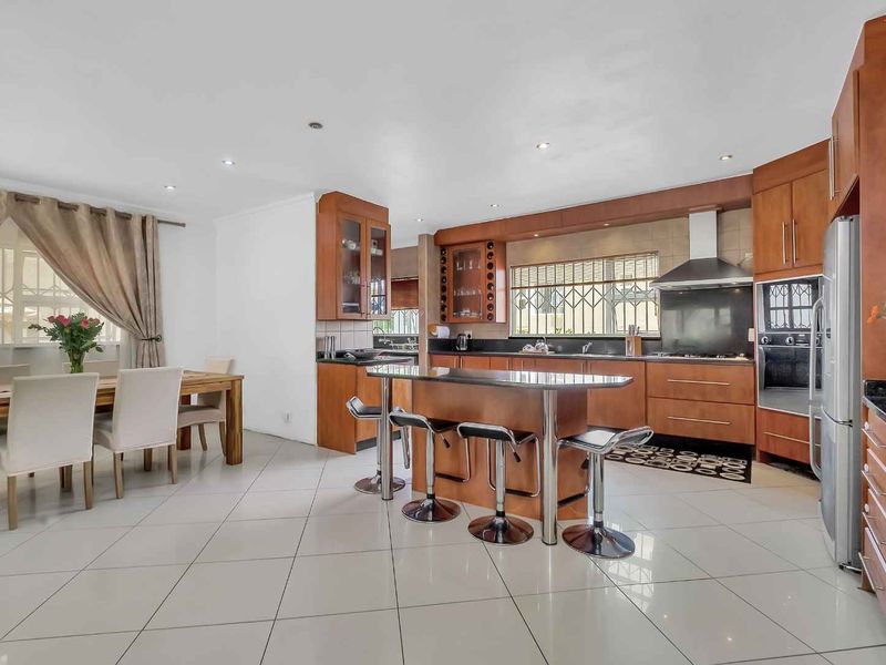 Spacious open-plan kitchen and dining area featuring wooden cabinetry, granite countertops, a central island, and tiled flooring throughout.