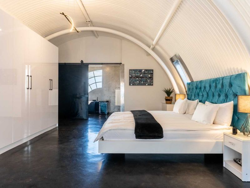 Modern bedroom featuring a unique curved corrugated metal ceiling, polished concrete floors, and extensive built-in white cabinetry with a sleek sliding door entry.