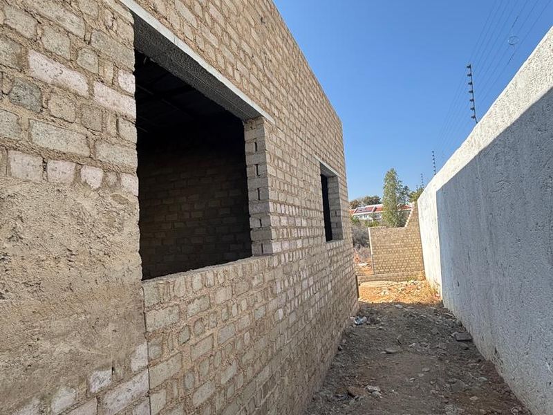 Side view of a property under construction, featuring exposed brick walls and an adjacent boundary wall with electric fencing.