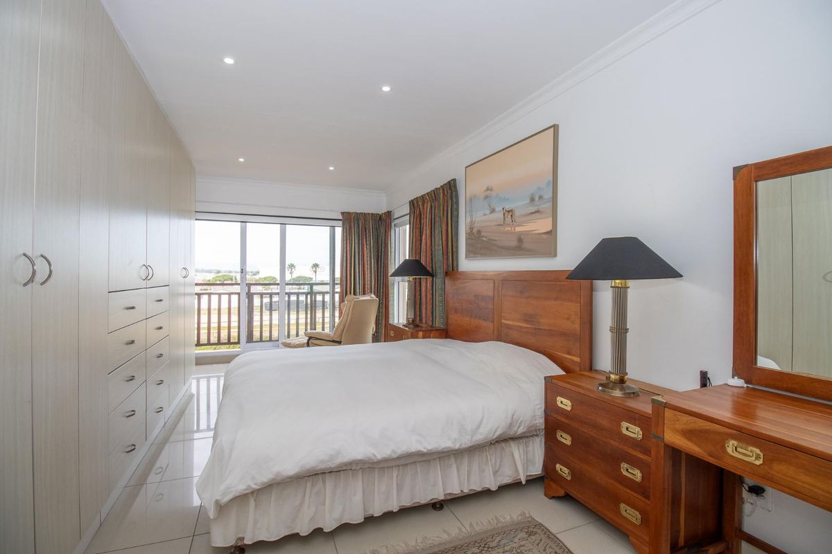 A well-maintained bedroom featuring extensive built-in cabinetry, tiled flooring, recessed lighting, and sliding glass doors leading to a private balcony.