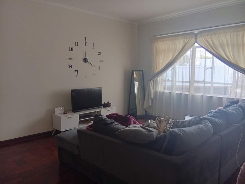 A living room featuring warm parquet flooring, a large window with natural light, and neutral wall finishes.