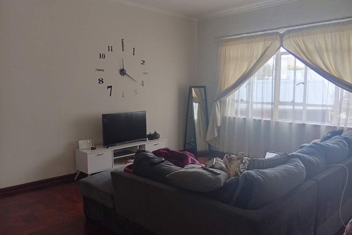 A living room featuring warm parquet flooring, a large window with natural light, and neutral wall finishes.