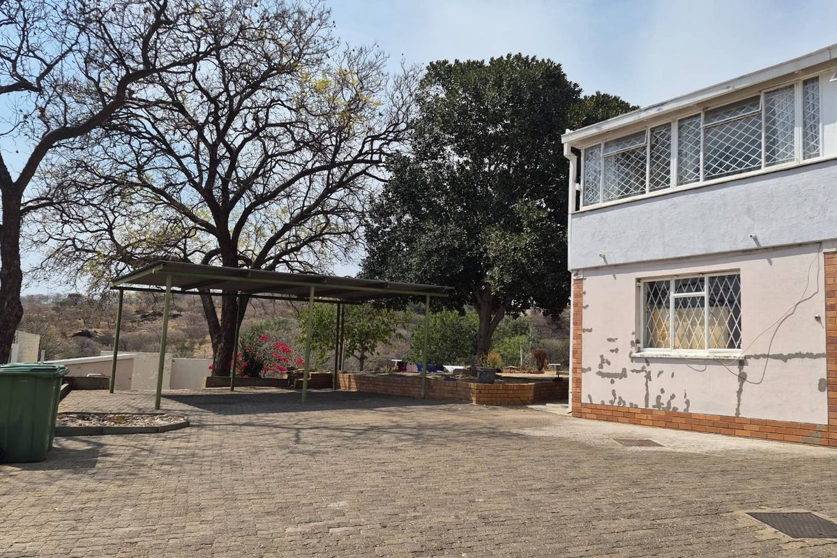 Rear exterior view of the property featuring a paved driveway, a metal carport, and mature trees, showing signs of exterior wall maintenance required.