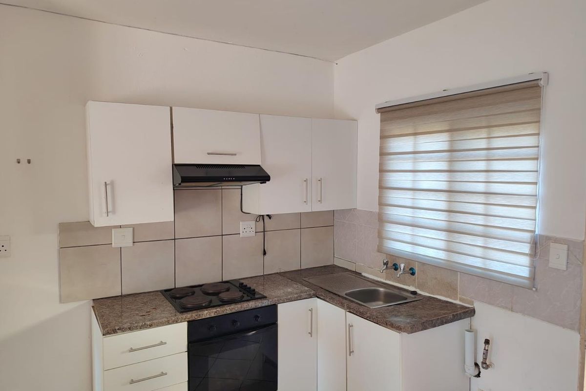 Compact kitchen featuring white cabinetry, granite countertops, built-in oven, electric hob, extractor fan, and a stainless steel sink with tiled backsplash.