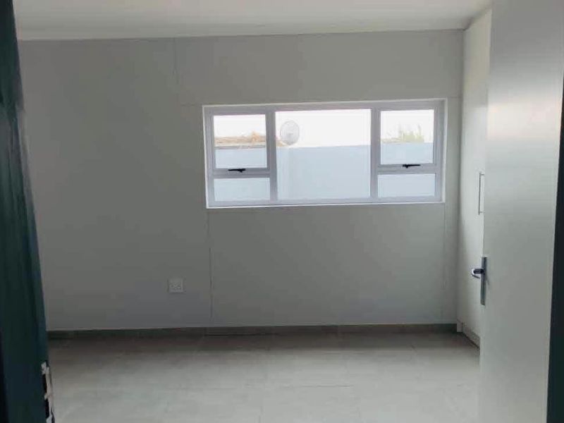 A clean, empty bedroom featuring neutral wall finishes, tiled flooring, and a built-in wardrobe with modern aluminium window frames.
