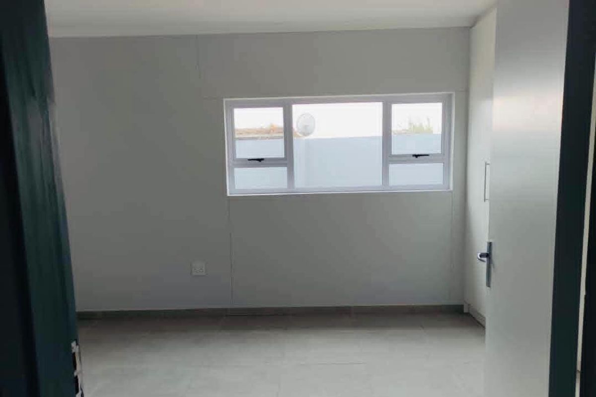 A clean, empty bedroom featuring neutral wall finishes, tiled flooring, and a built-in wardrobe with modern aluminium window frames.