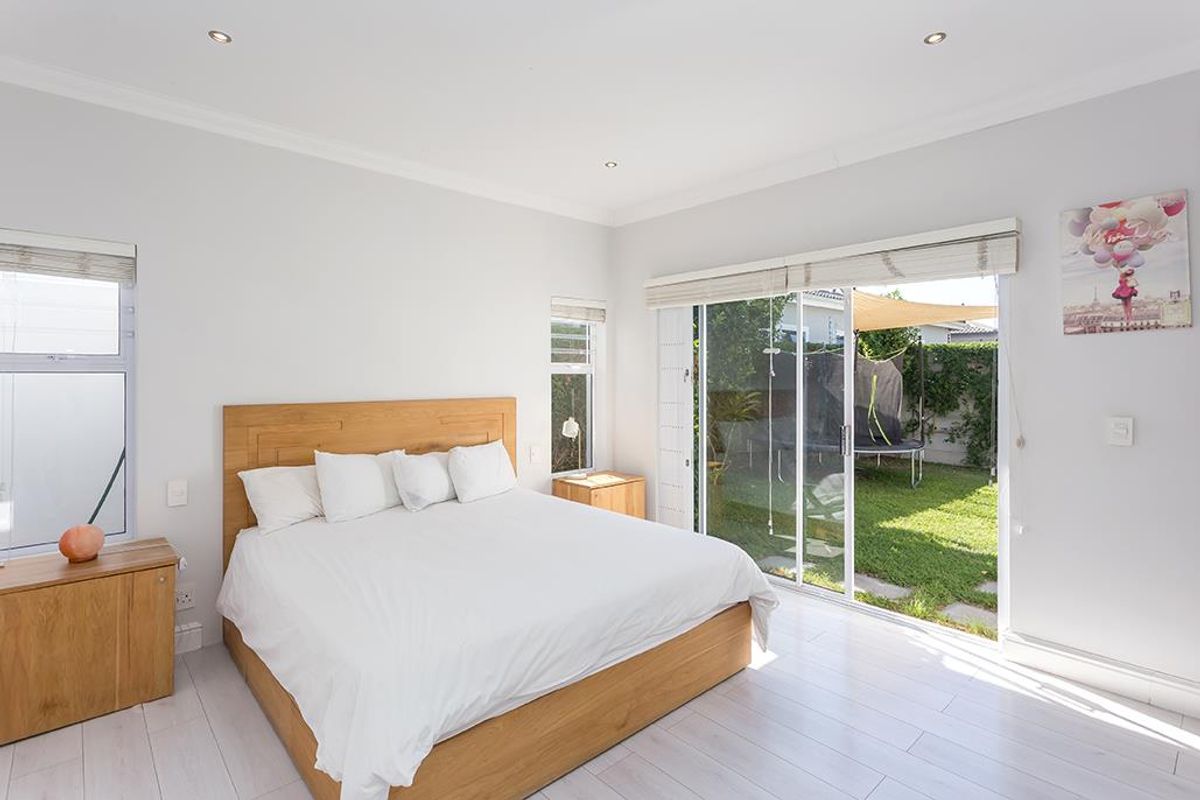 Bright bedroom featuring timber-look flooring, recessed downlights, and large sliding glass doors providing direct access to the rear garden.