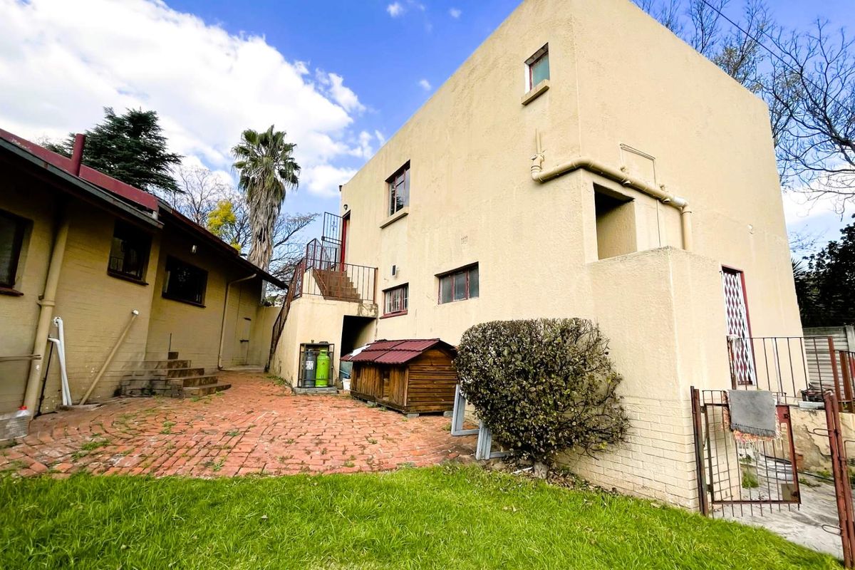 Rear view of the property featuring a brick-paved courtyard, external staircase, and multi-level exterior walls with established garden surroundings.