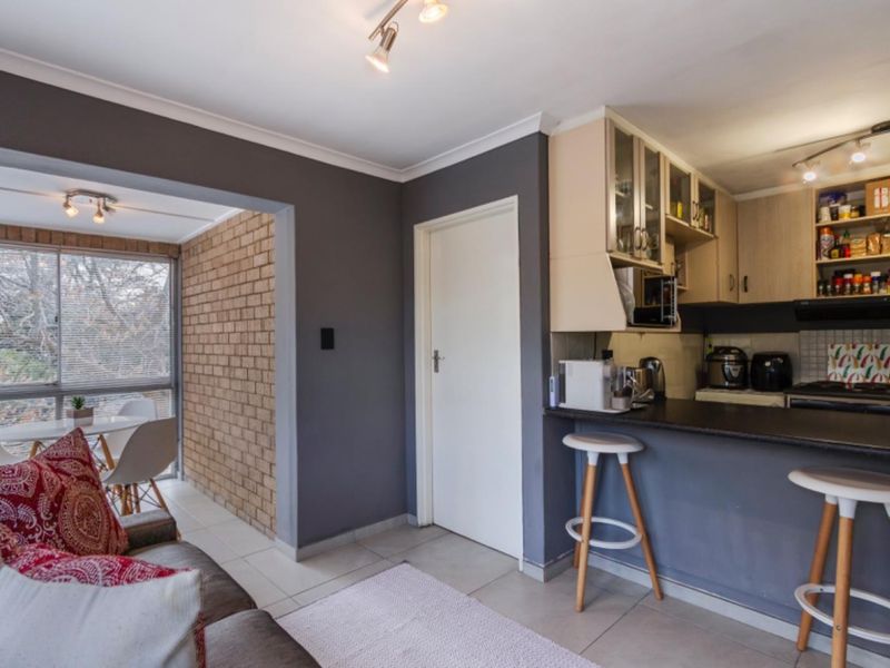 Open plan living area featuring a kitchen with breakfast bar, tiled flooring, and an adjacent sunroom with exposed brick wall detail.