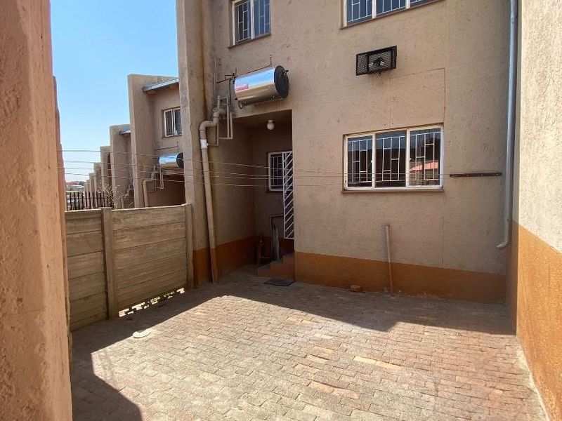 Rear exterior view of the townhouse featuring a private brick-paved courtyard, solar geyser installation, and secure window fittings.