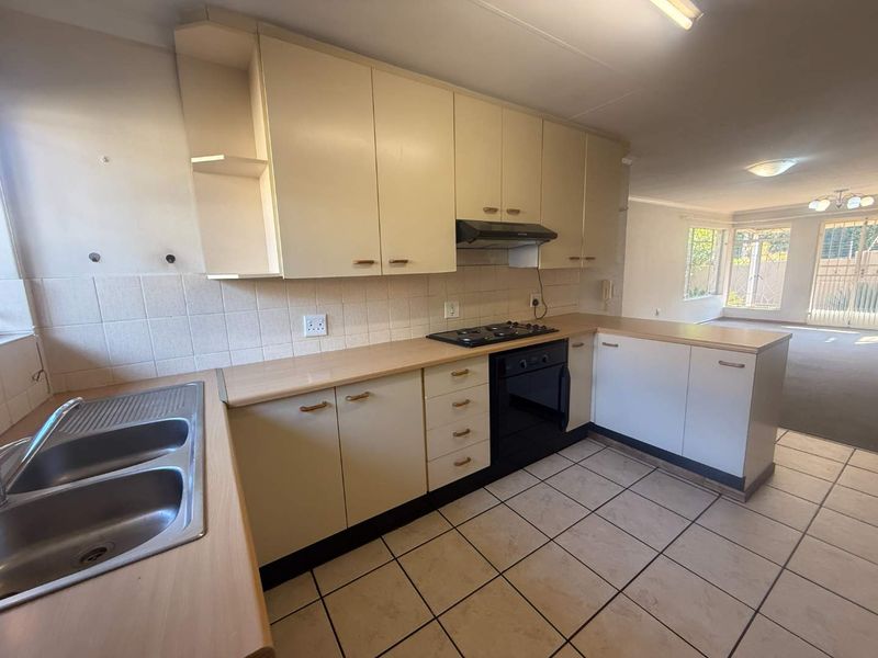 A functional, open-plan kitchen featuring built-in cabinetry, a gas hob, oven, and double sink, flowing directly into the adjacent living area.