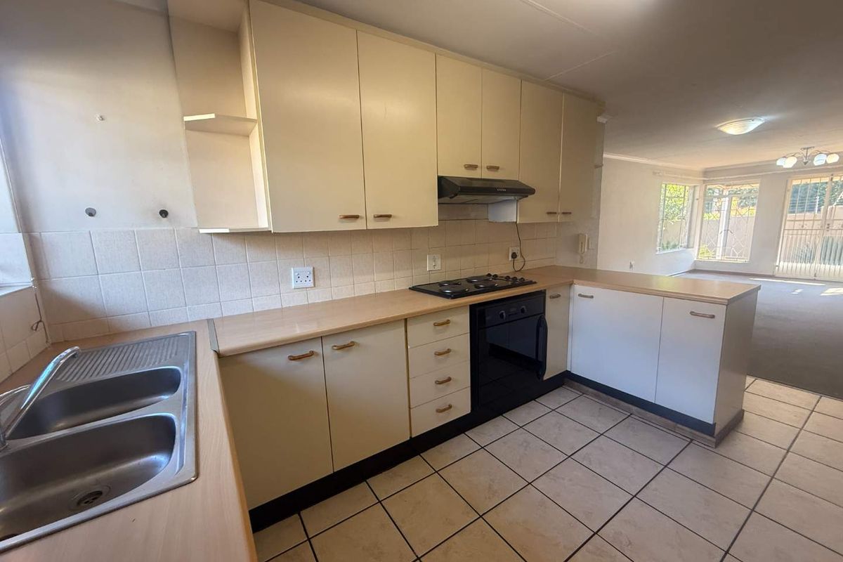 A functional, open-plan kitchen featuring built-in cabinetry, a gas hob, oven, and double sink, flowing directly into the adjacent living area.