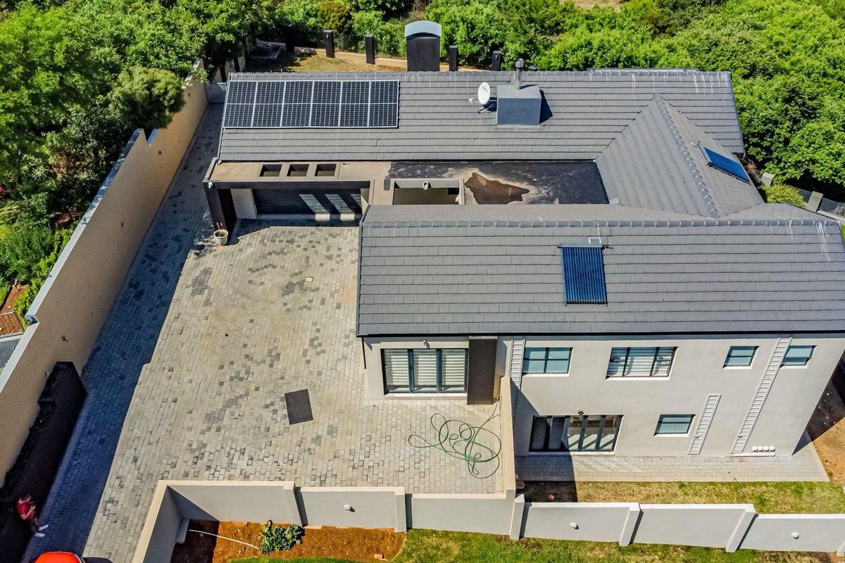 Aerial view of the property featuring a tiled roof, solar panels, solar water heating system, paved driveway, and perimeter boundary walls.
