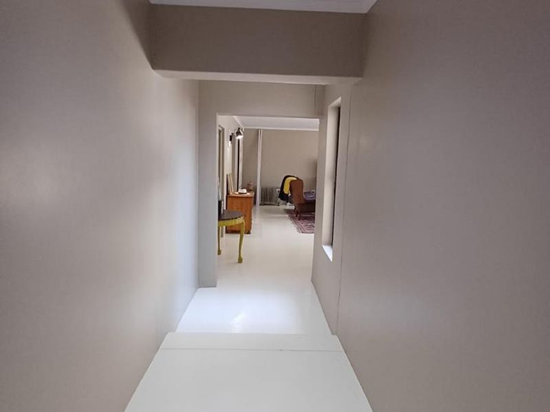 A clean, neutral-toned hallway featuring recessed lighting and smooth finishes, leading into an adjacent living space.