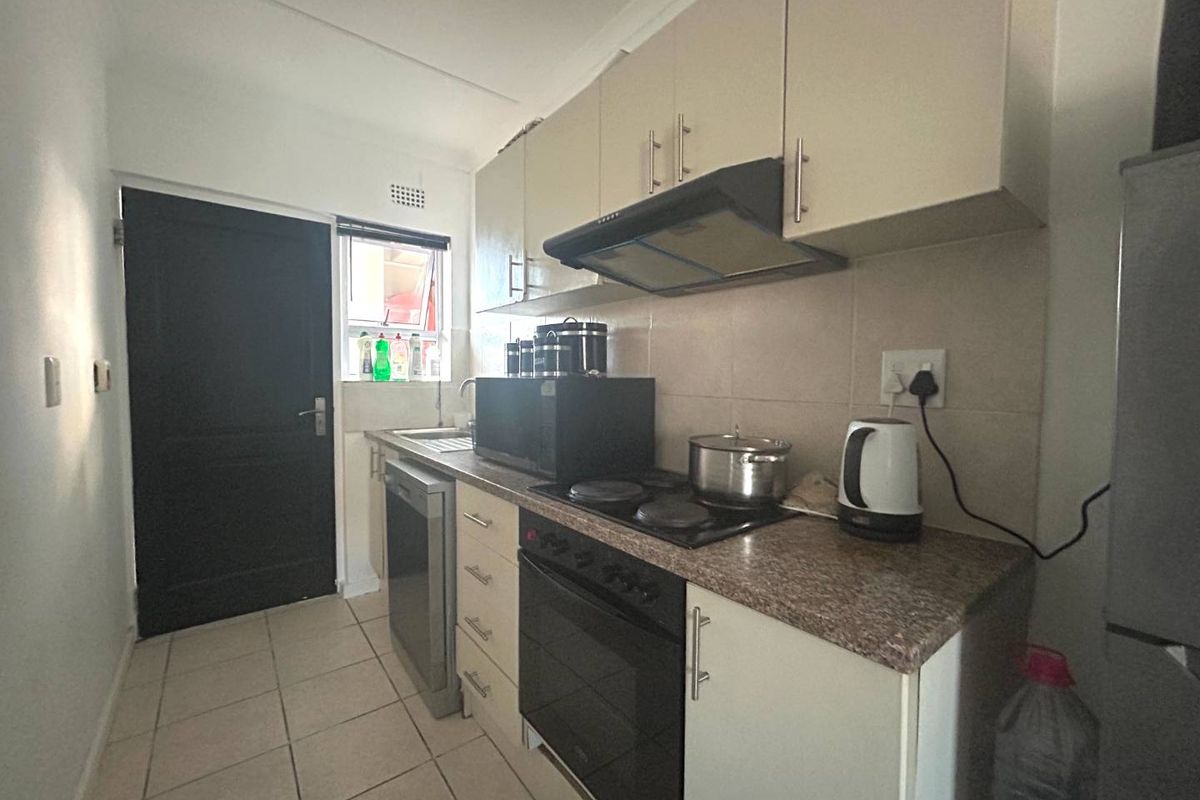 Compact kitchen featuring neutral cabinetry, a built-in oven with electric hob, extractor fan, and tiled flooring with direct access to an exterior door.