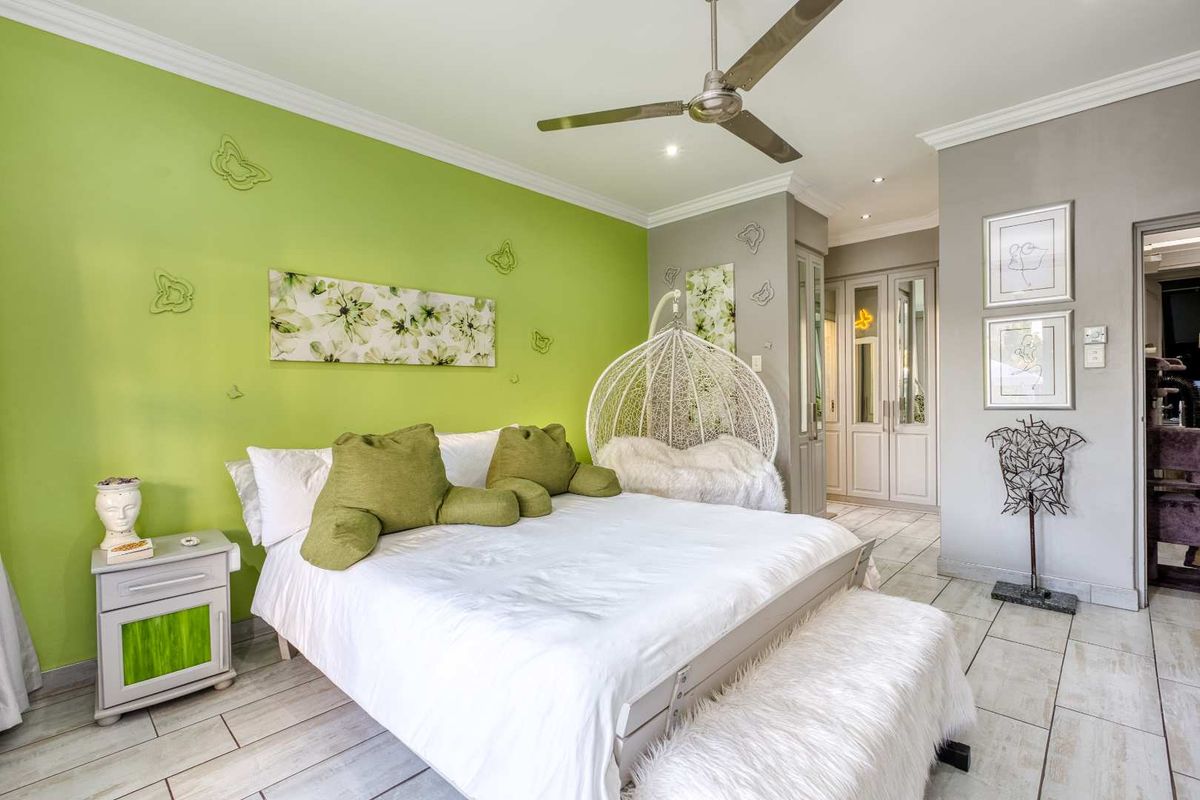 A well-maintained bedroom featuring tiled flooring, built-in cupboards, and a ceiling fan, finished with a vibrant accent wall.