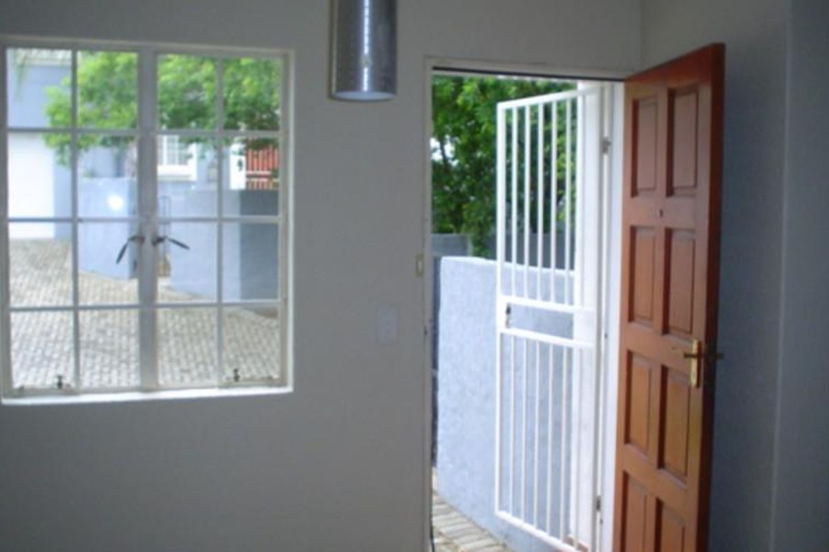 An empty living area featuring a timber entrance door, security gate, and a window with burglar bars looking out onto the driveway.