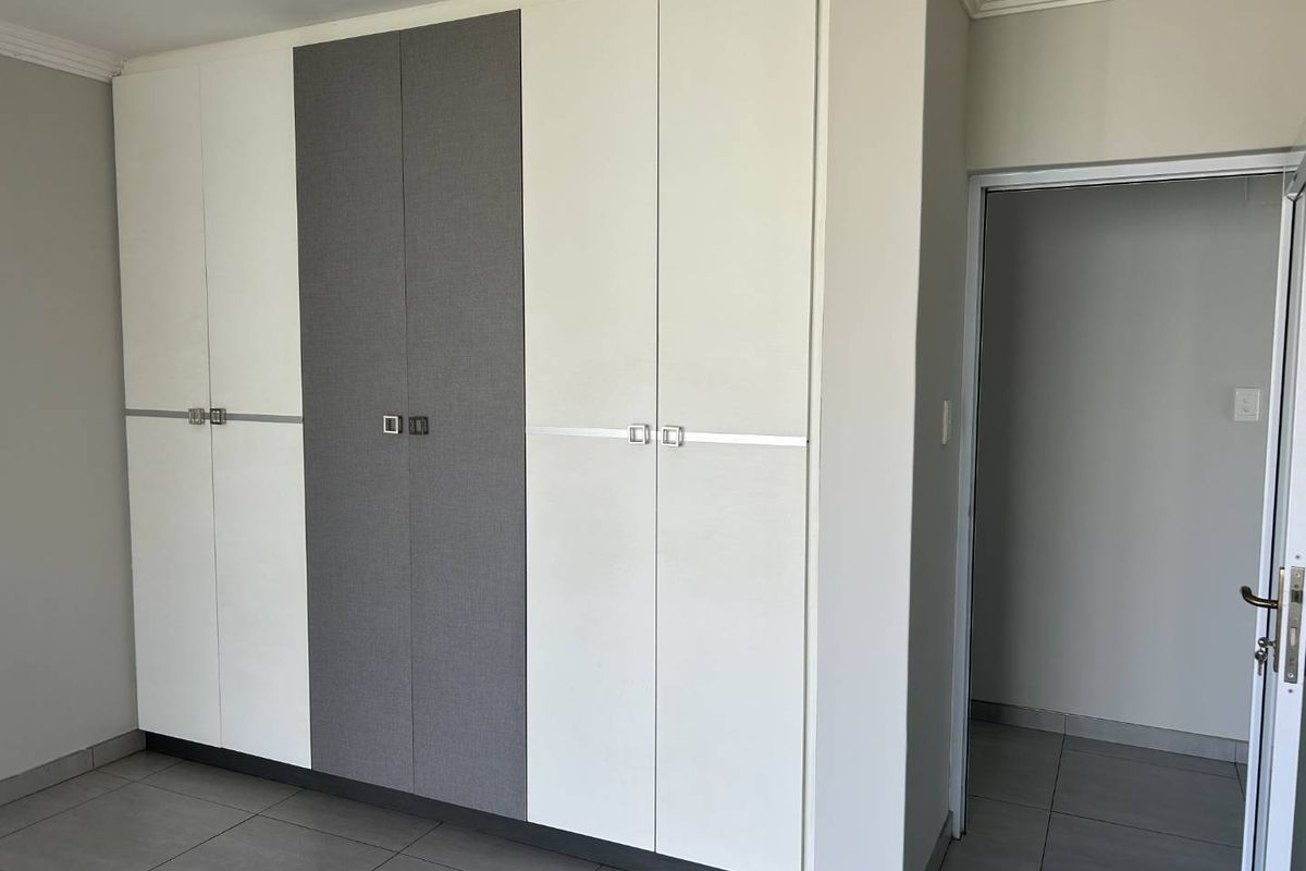 A bedroom featuring modern, floor-to-ceiling built-in wardrobes with a two-tone white and grey finish and tiled flooring.