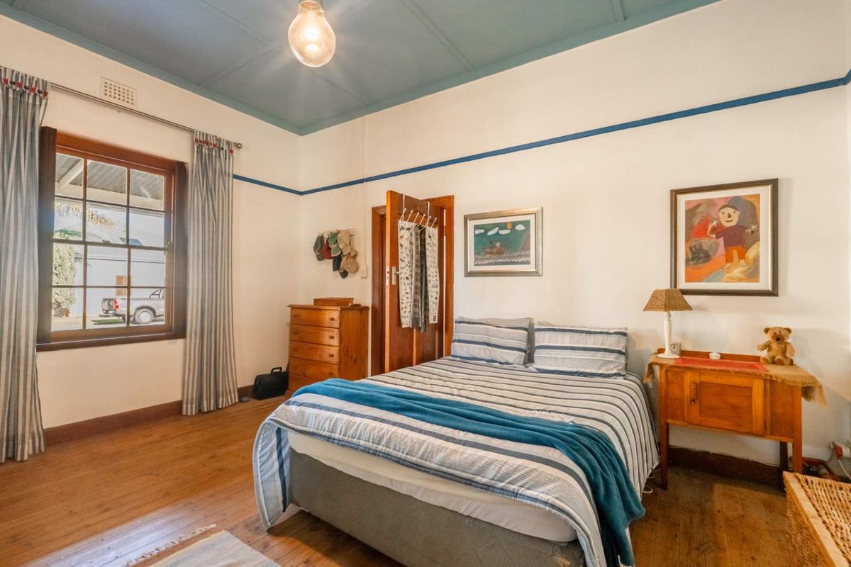 A bedroom featuring original timber flooring, high ceilings with decorative trim, and a large window allowing natural light.