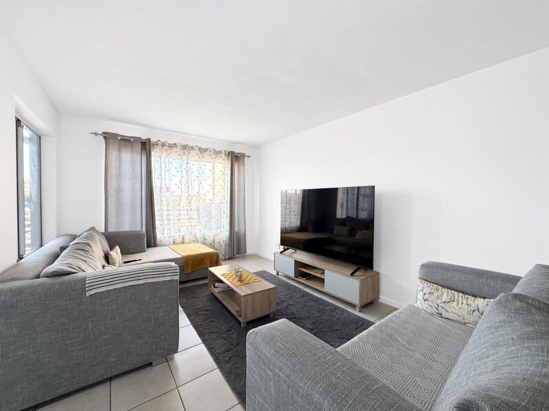 A bright and well-maintained living room featuring neutral tiled flooring and a large window that allows for ample natural light.
