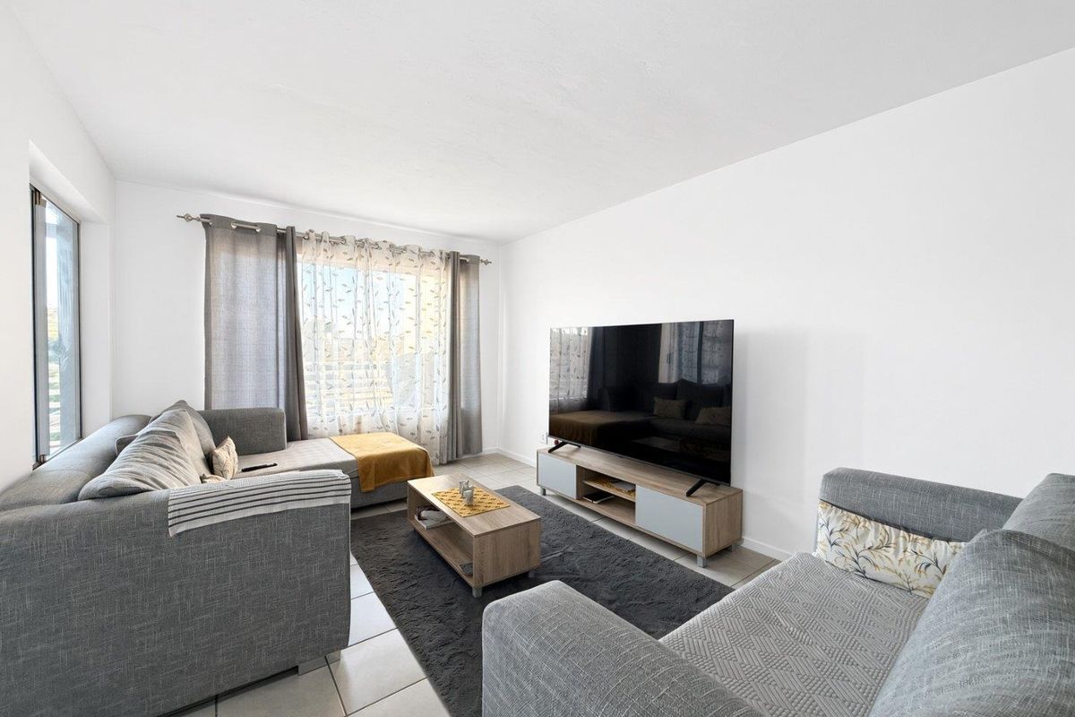 A bright and well-maintained living room featuring neutral tiled flooring and a large window that allows for ample natural light.