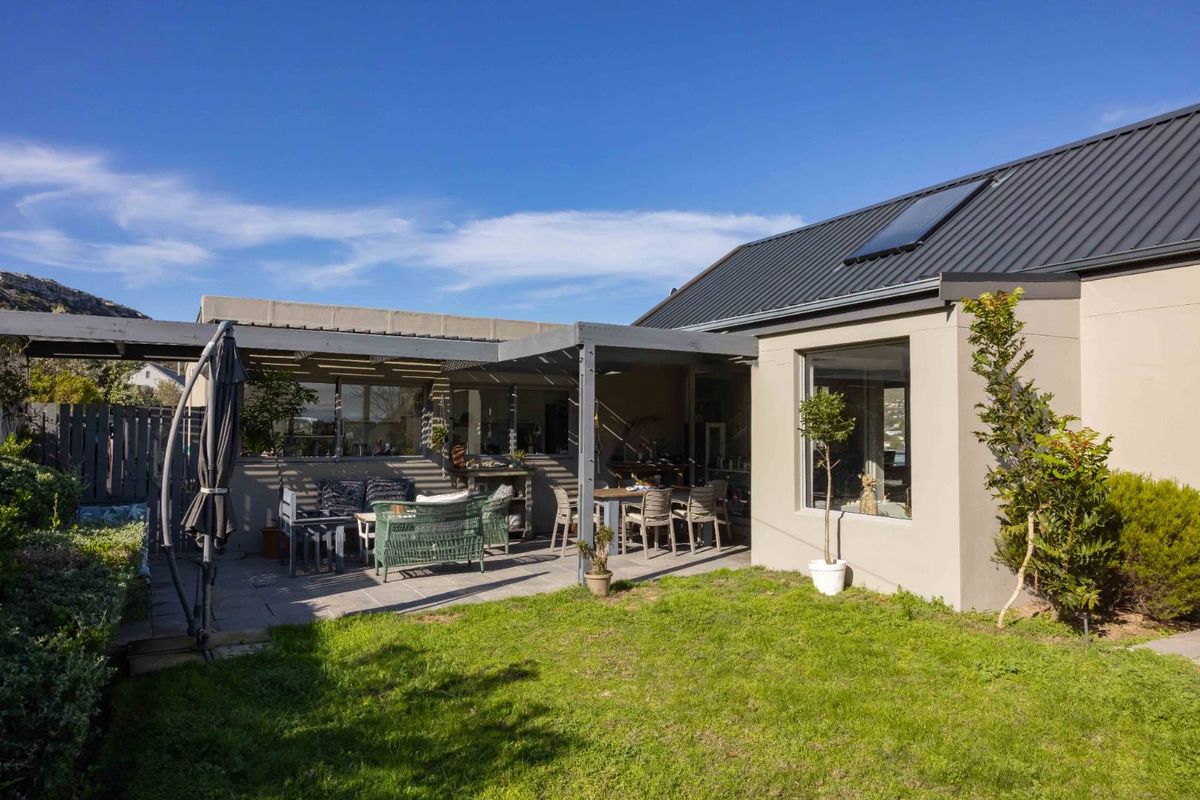 Rear view of the property featuring a covered patio area, paved terrace, and a well-maintained lawn with a metal roof and solar water heater.