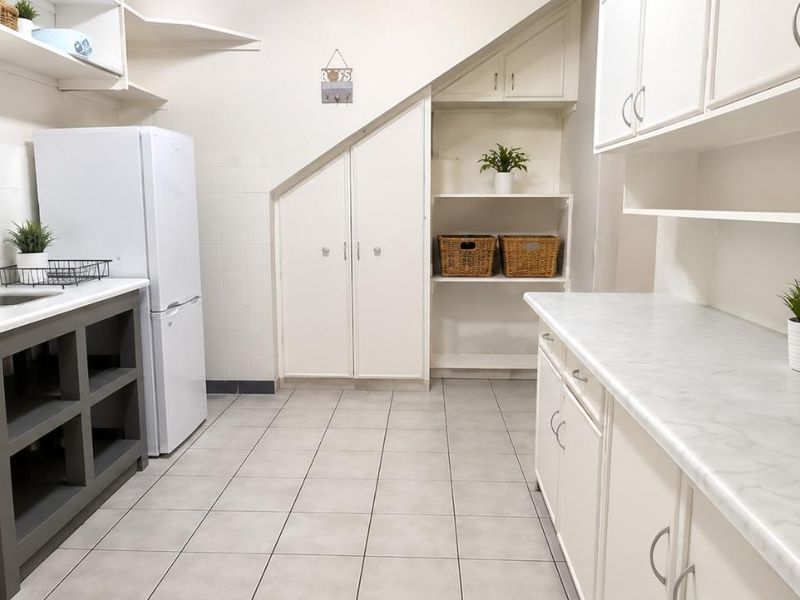 A functional scullery area featuring built-in cabinetry, laminate countertops, a stainless steel sink, and practical under-stair storage with tiled flooring.