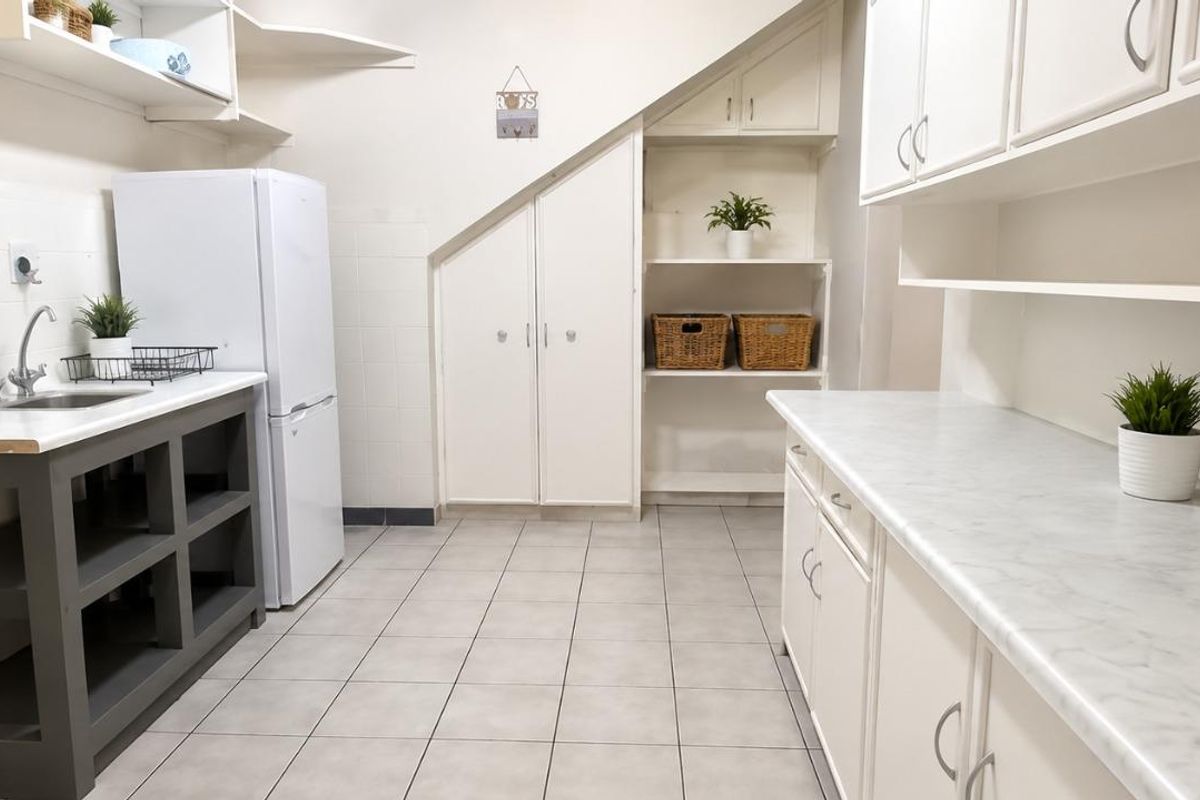 A functional scullery area featuring built-in cabinetry, laminate countertops, a stainless steel sink, and practical under-stair storage with tiled flooring.