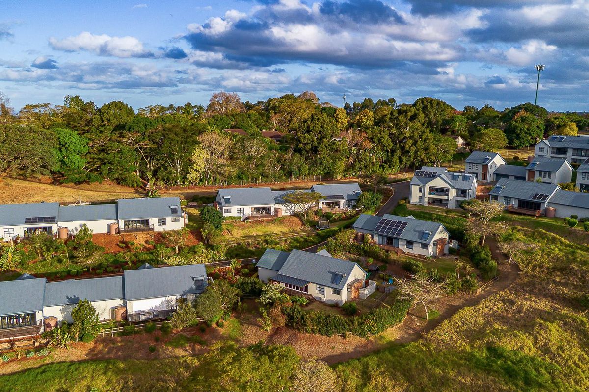 An aerial view of a townhouse complex featuring multiple units with metal roofs, solar panels, and established landscaped surroundings.