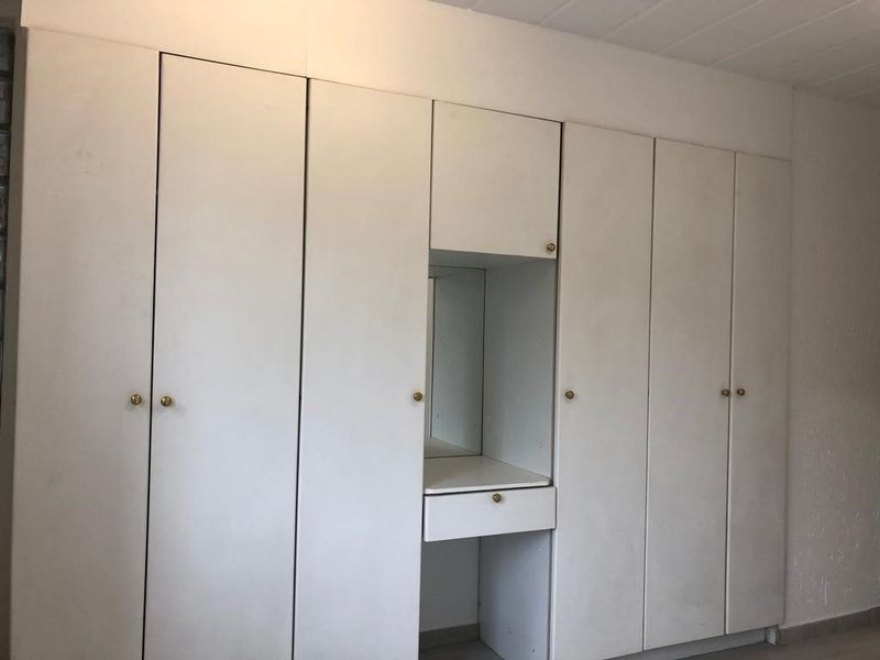 A bedroom featuring a large wall-to-wall built-in cupboard unit with an integrated vanity and mirror, offering ample storage space.