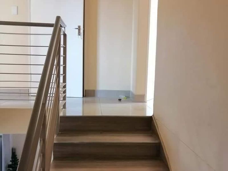 A clean, modern staircase featuring wood-look treads and a stainless steel balustrade, leading to an upper landing with tiled flooring.