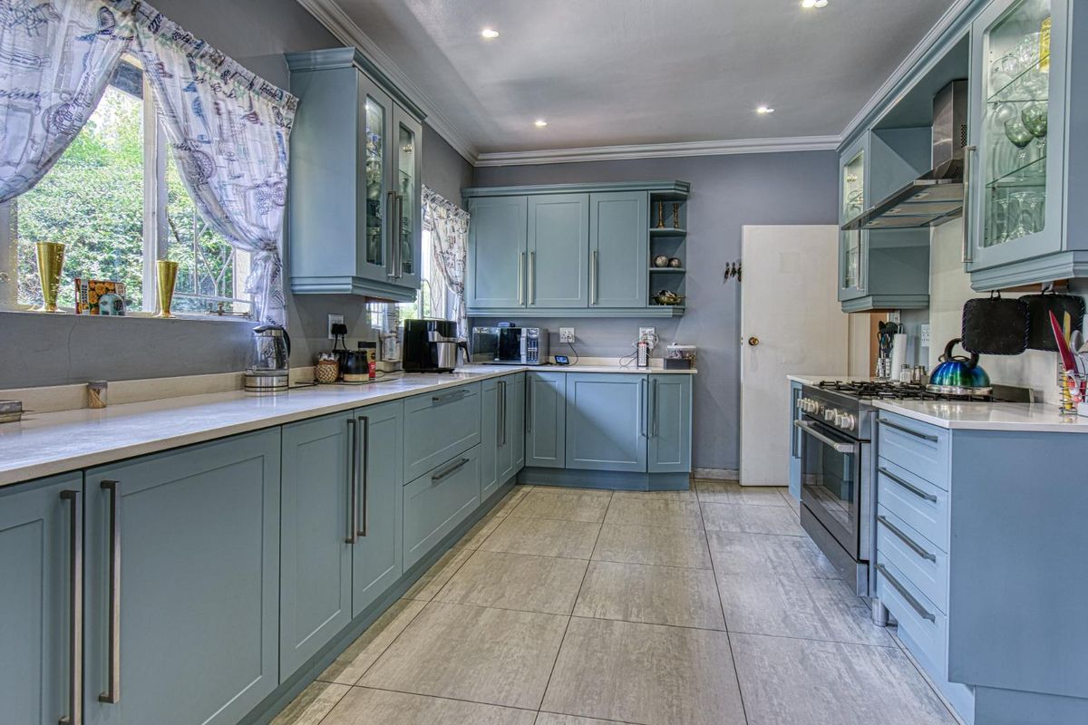 A well-maintained kitchen featuring light blue cabinetry, stone countertops, tiled flooring, and a built-in stainless steel oven and extractor fan.