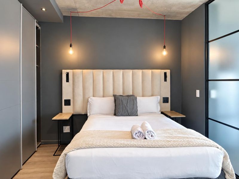 Modern bedroom featuring an exposed concrete ceiling, built-in wardrobe, stylish pendant lighting, and a sleek sliding glass partition wall.