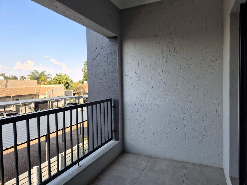 A clean, covered balcony featuring tiled flooring, a metal balustrade, and textured wall finishes, offering an open outdoor space.