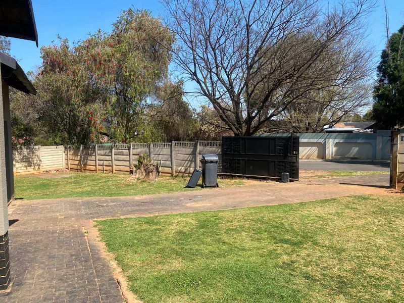 A rear garden area featuring a paved driveway, precast concrete boundary wall, and a metal sliding gate leading to the street.