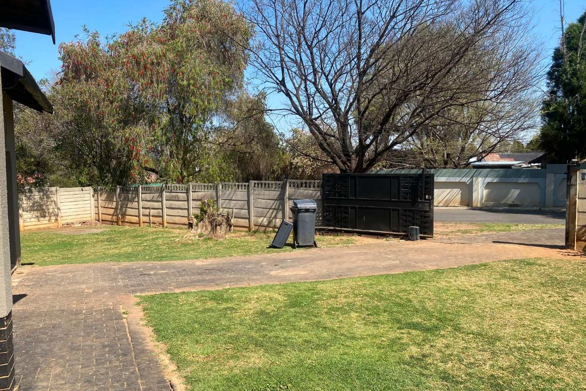 A rear garden area featuring a paved driveway, precast concrete boundary wall, and a metal sliding gate leading to the street.