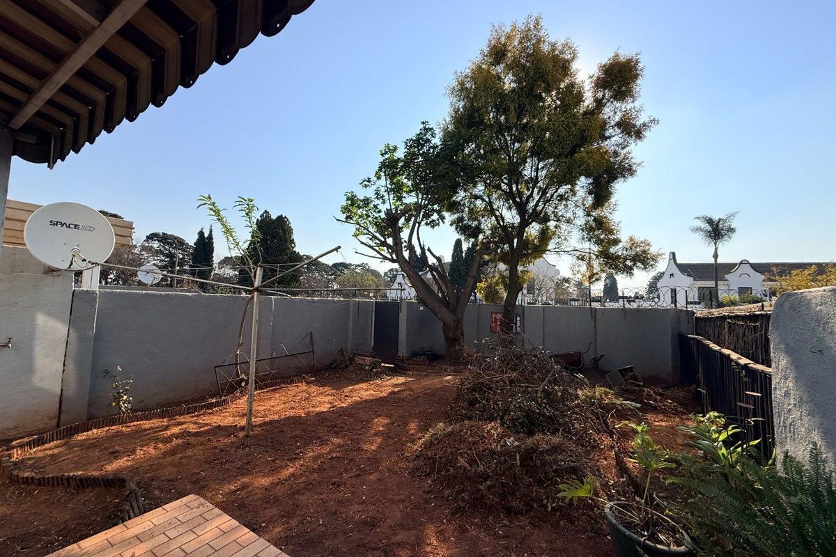 A rear garden area featuring a boundary wall with security spikes, brick paving, and an open yard space requiring landscaping.