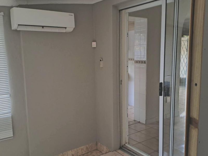 An empty living area featuring tiled flooring, a wall-mounted air conditioning unit, and a sliding glass door leading to an adjacent tiled space.