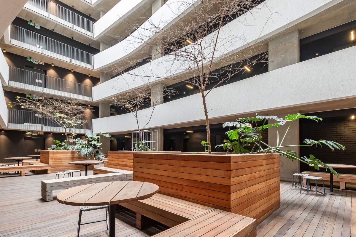 A modern, multi-level apartment complex atrium featuring a central courtyard with timber decking, built-in wooden planters, and open-air walkways.