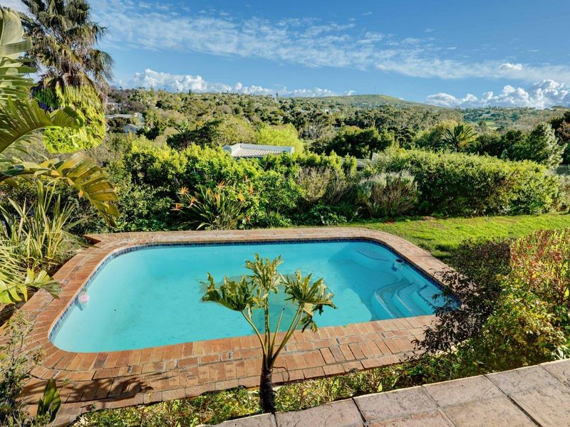 A well-maintained swimming pool with brick coping, set within a lush garden featuring scenic hillside views.