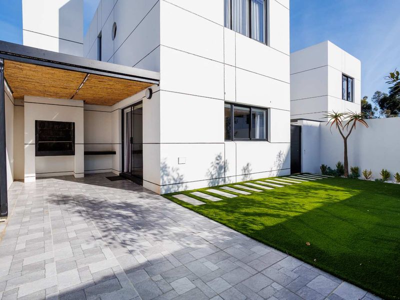 Modern rear exterior featuring a paved patio with a built-in braai, covered pergola, and a well-maintained artificial lawn area.