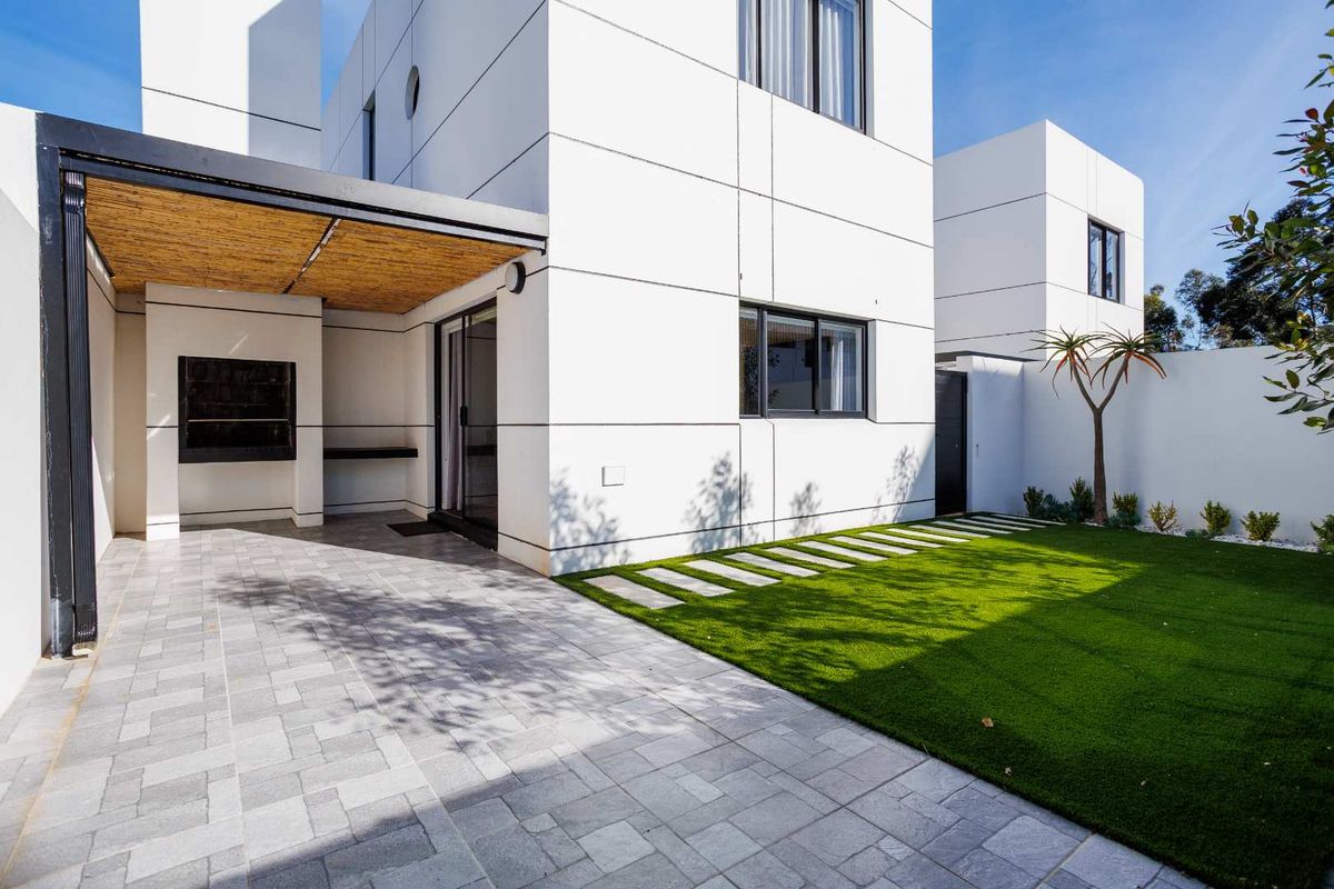Modern rear exterior featuring a paved patio with a built-in braai, covered pergola, and a well-maintained artificial lawn area.