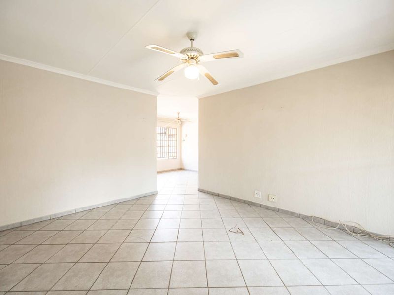 An empty, open-plan living area featuring neutral walls, ceramic tiled flooring, and a central ceiling fan, offering a blank canvas for interior design.